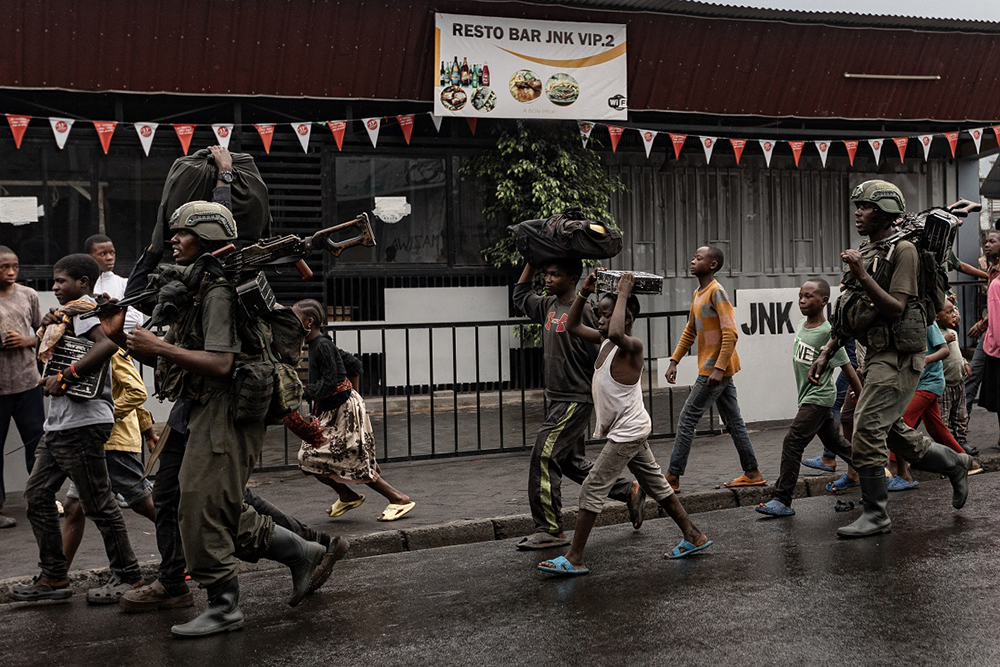 Members of the M23 armed group walk alongside residents through a street of the Keshero neighborhood in Goma, on January 27, 2025. (Credit: AFP)