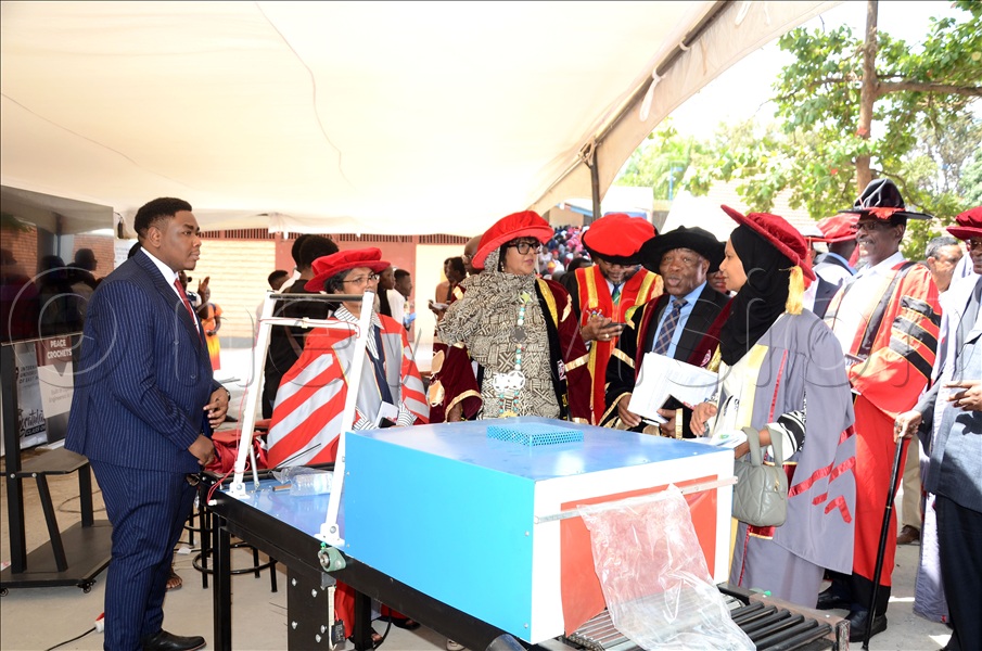 Gael Ongor Iko (L), one of the innovators of the packaging machine, explaining to officials of the International University of East Africa (IUEA) and guests how it was built and how it is used. This was during the 12th graduation ceremony of the International University of East Africa at the main campus in Kampala on November 27, 2025.