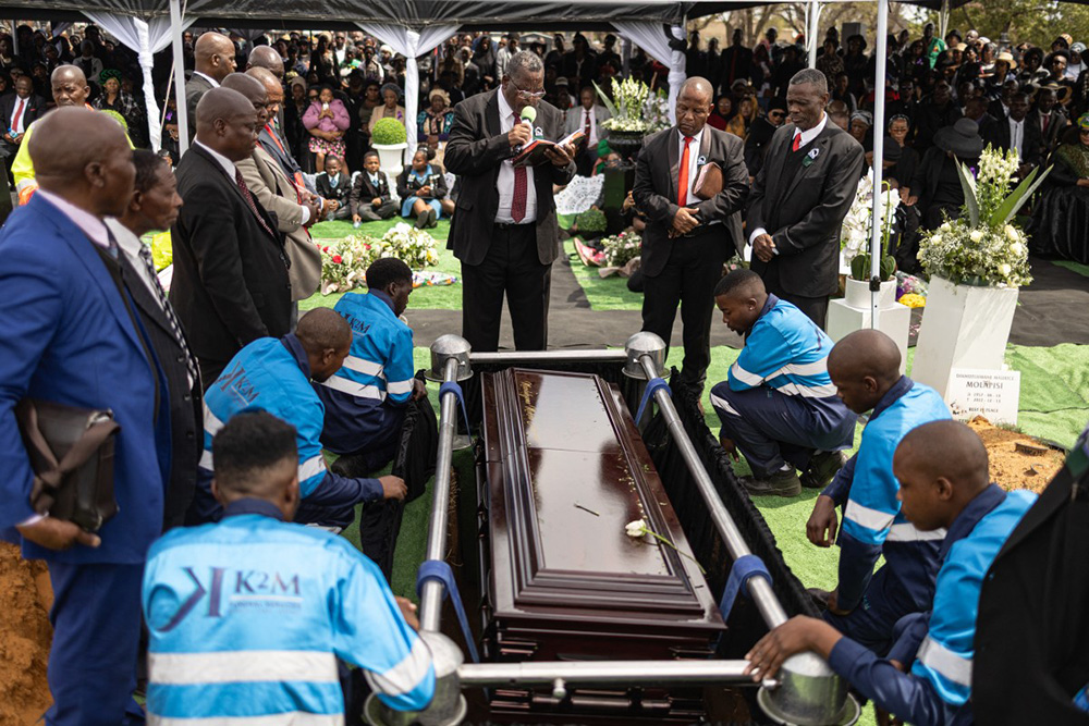 A Zion Christian Church (ZCC) member reads from the Bible as the coffin of Elizabeth “Tsontso” Mokolo Moselakgomo, a victim of the recent east Johannesburg murders, is lowered into the ground during her funeral service in Mpumalanga on September 20, 2026. (Photo by EMMANUEL CROSET / AFP)