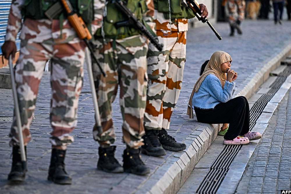 Indo-Tibetan Border Police (ITBP) personnel stand guard near closed shops as a girl enjoys a chocolate along a pavement after curfew was partially relaxed for a few hours in Leh on September 27, 2025