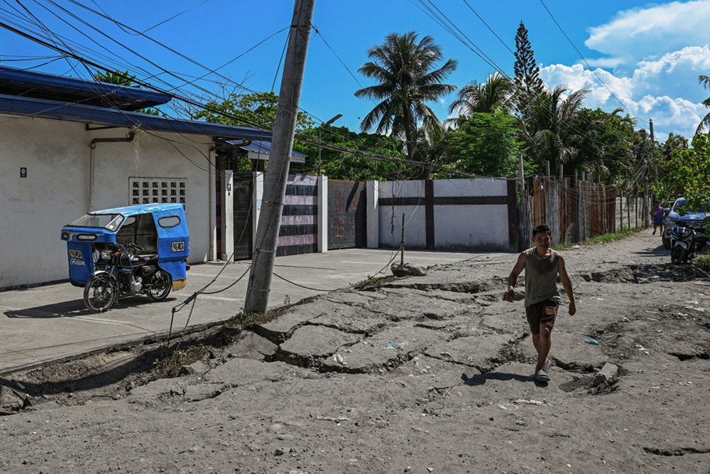 A man walks along a damaged road after a 7.8 magnitude earthquake in General Santos City on June 9, 2026. (Photo by Jam STA ROSA / AFP)