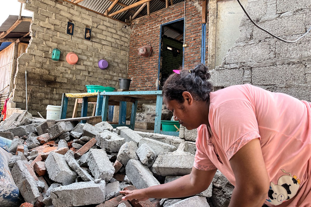 A resident clears debris from a damaged wall of her home after a shallow 4.9 magnitude earthquake in Adonara, East Nusa Tenggara on April 9, 2026, damaging dozens of homes and injuring multiple people, an official said. (Photo by Handrianus Hali / AFP)