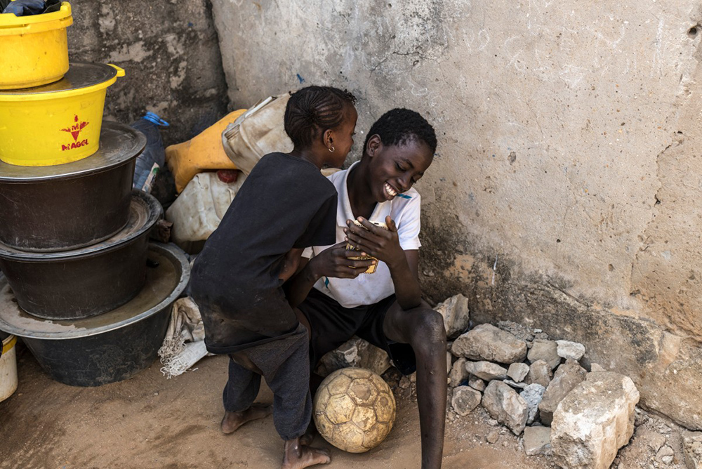 Coumba (L) plays with her brother Boubacar (R) outside their home in Mbour, on March 9, 2026. Both siblings lost their father in 2022 as the pirogue he was travelling in capsized trying to reach Europe through the Atlantic route. (Photo by PATRICK MEINHARDT / AFP)