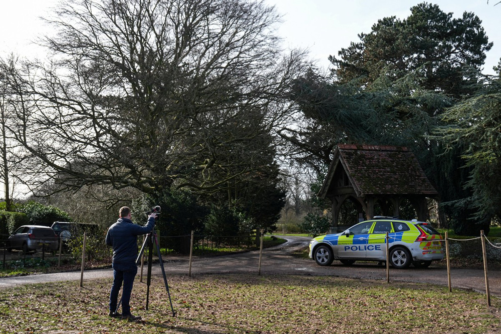 A journalist (L) monitors a police vehicle at an entrance to Wood Farm on the royal family's Sandringham Estate in Norfolk, eastern England on February 22, 2026, after Britain's former prince Andrew was arrested on February 19. (Photo by CARLOS JASSO / AFP)