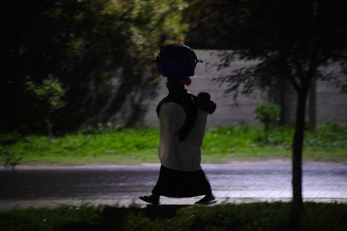 An immigrant carrying her child and belongings walks to a community hall in Stanford, about 120km from Cape Town, on June 2, 2026, after they were threatened in the communities in which they live. (Credit: AFP)