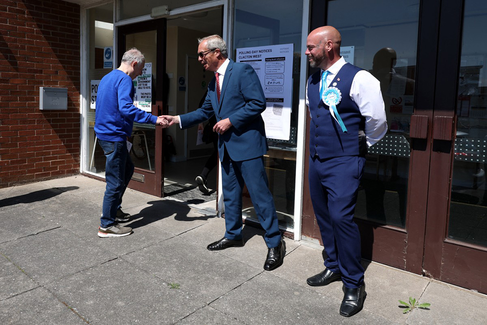 Reform UK leader Nigel Farage and Reform councillor for West Clacton and Jaywick Sands, Bradley Thompson (R) greet a voter outside a polling station in Jaywick, near Clacton-on-Sea, eastern England on May 7, 2026. 