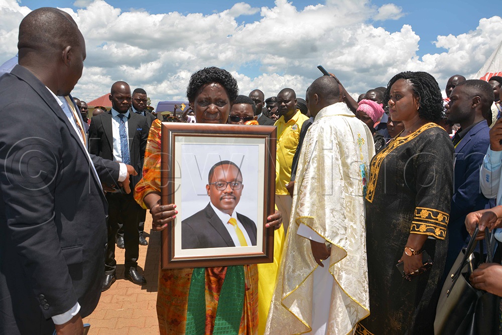 Janipher Namuyangu, the Minister of State for Bunyoro Affairs, holding the portrait of the deceased Banura and other leaders as they received Banura’s body. (Photo by Peter Abaanabasazi)