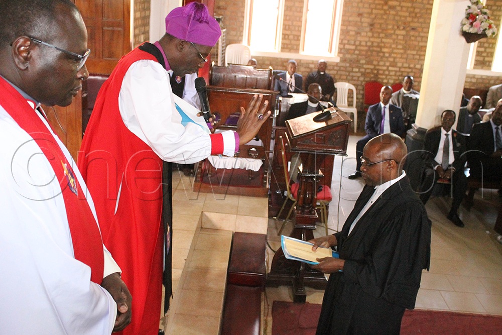 Bishop Fred Sheldon Mwesigwa of Ankole Diocese blesses Benson Tusasiirwe, the newly appointed diocesan chancellor, as Ankole Diocese Secretary Rev Canon Edson Abaasa looks on. (Photo by Abdulkarim Ssengendo)