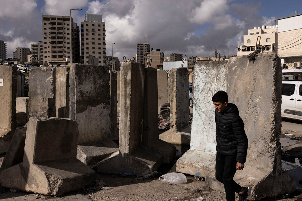 A Palestinian man walks past concrete blocks at the Israeli-controlled Qalandiya checkpoint in the occupied West Bank on February 11, 2026.
