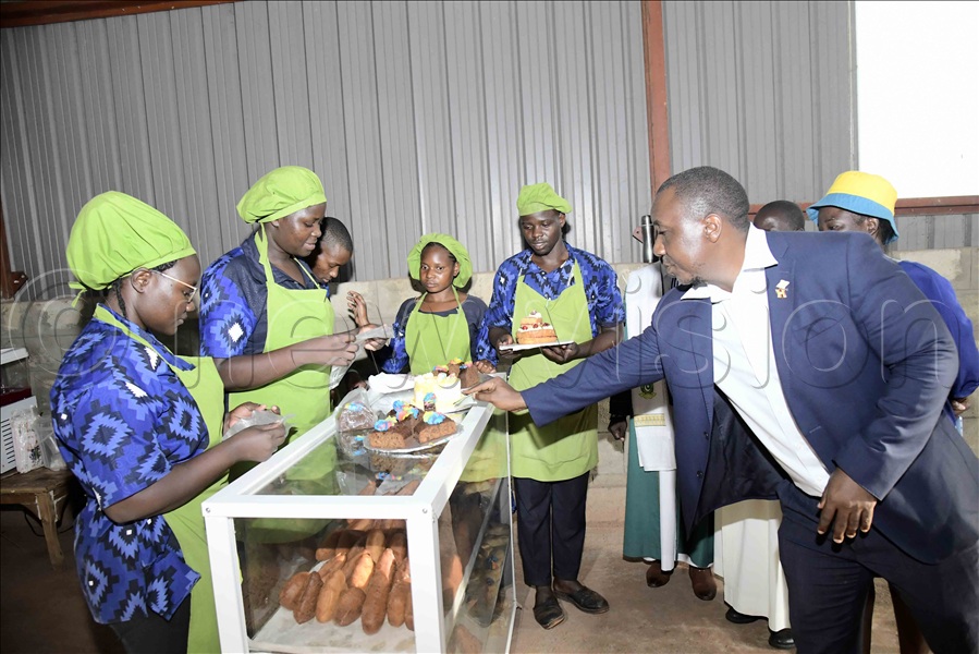 Assistant RDC Bugweri District, Abdu Luzze, picking some of the snacks made by trainees from the Busoga Presidential Skilling Hub during a hub tour.