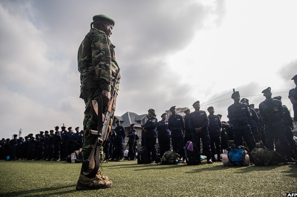 A member of the M23 movement stands guard as Congolese police officers arriving from Bukavu line up during an enrollment of civilians, police officers, and former members of the Armed Forces of the Democratic Republic of Congo (FARDC) who allegedly decided to join the M23 movement voluntarily in Goma on February 23, 2025