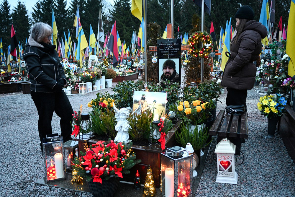 People visit the grave of a fallen Ukrainian soldier decorated with Christmas trees and New Year's decorations at the Lychakiv Military Cemetery on the day before Christmas Eve, in Lviv, amid the Russian invasion of Ukraine. 