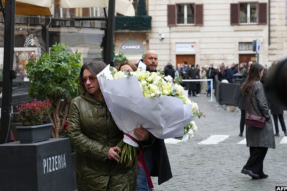 A woman holds a bouquet of white flowers as she arrives at the PM23 exhibition site where late Italian fashion designer Valentino Garavani is lying in state before the funeral, in Rome.