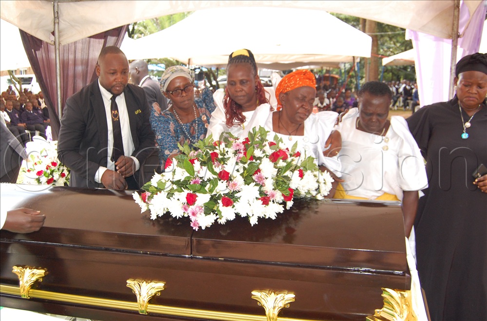 ViFr. Muvunyi's mother (fourth-left) being supported by relatives as she lays a wreath on the casket bearing his remains.
