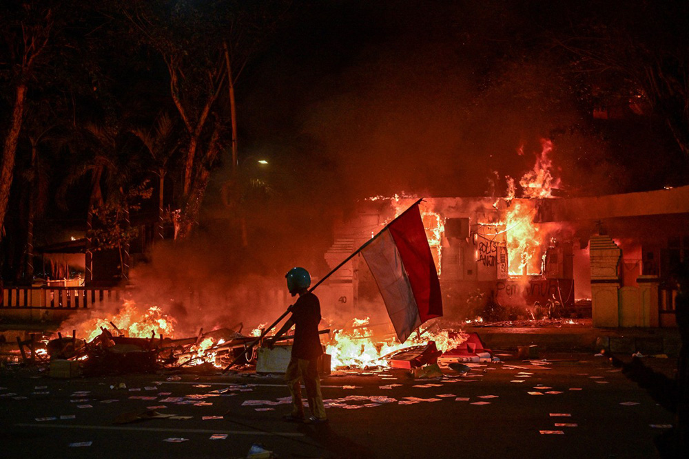 A protester walks with an Indonesian flag in front of a police headquarters that was set on fire and looted during demonstrations in Surabaya on August 31, 2025. (Photo by Juni KRISWANTO / AFP)