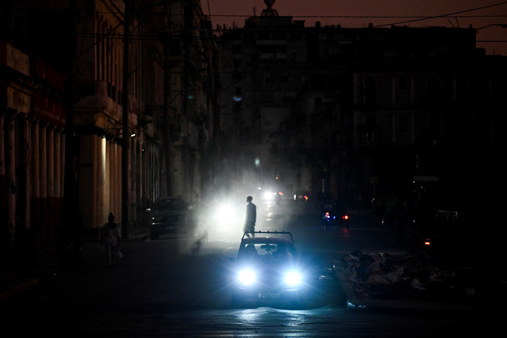 A man walks while cars cruise along a street during a blackout in Havana on March 16, 2026. (AFP)