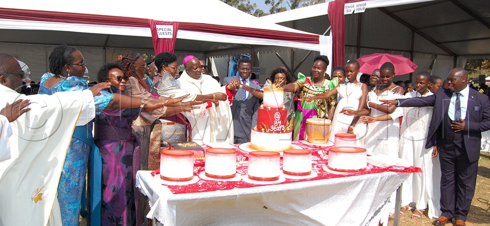 Bishop Serverus Jjumba (wearing a skull-cap) joins Katikkiro Charles Peter Mayiga (wearing a grey suit) and other stakeholdres in the cutting of the cake. (Photo by Mathias Mazinga)