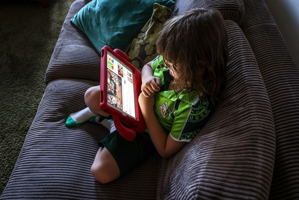 (FILES) This photo taken on October 30, 2025 shows six-year-old Enrique Navarro sitting on a couch with his iPad watching a show on YouTube at his home in western Sydney. (AFP)