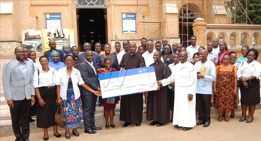 Members of the ministry of the grand-parents and the elderly presenting their dummy cheque to members of Lubaga Cathedral Centenary Organising Committee, who include  Msgr. Rogers Kabuye  (wearing a black cassock),  Michael Ssebbowa ( on Msgr. Kabuye's immediate right) and Fr. Achilles Mayanja (wearing a white cassock). Extreme left is John Kiyimba Freeman.   