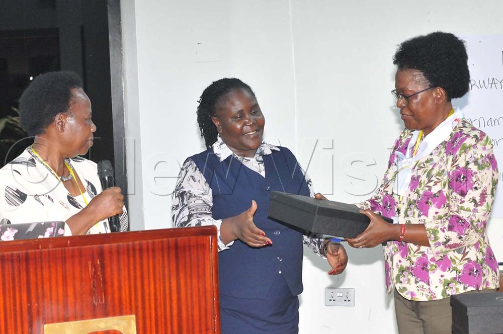 Sarah Bunoti (R), the Vice President Association of University Women Uganda hands over a gift to Rosette Nanyanzi, the Gender Technical Advisor at the education ministry as Getrude Ssekabira, association's president looks on. (Credit: Nicholas Oneal)