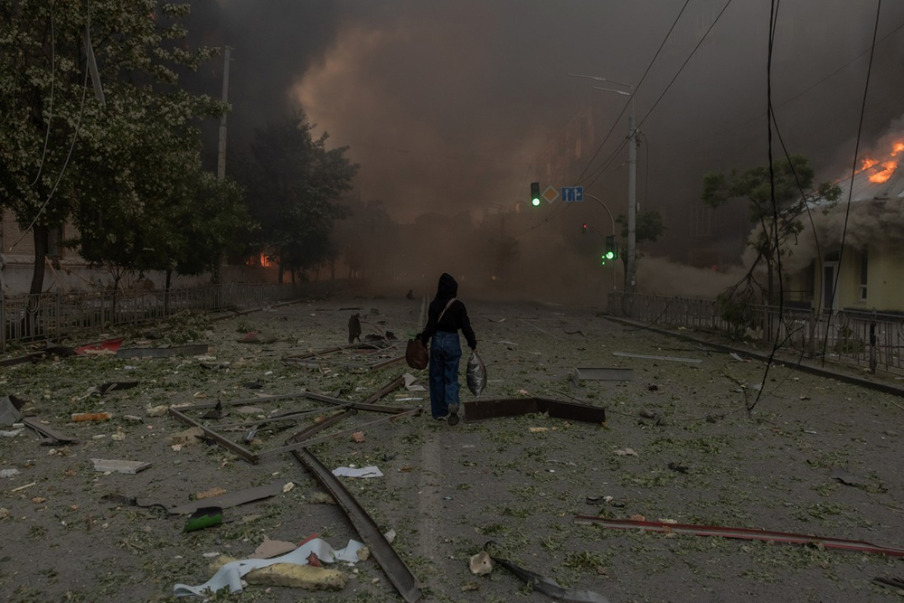 UkA woman walks along a smoke-filled road beside heavily damaged buildings following Russian strikes in Kyiv on May 24, 2026, amid the Russian invasion of Ukraine. 