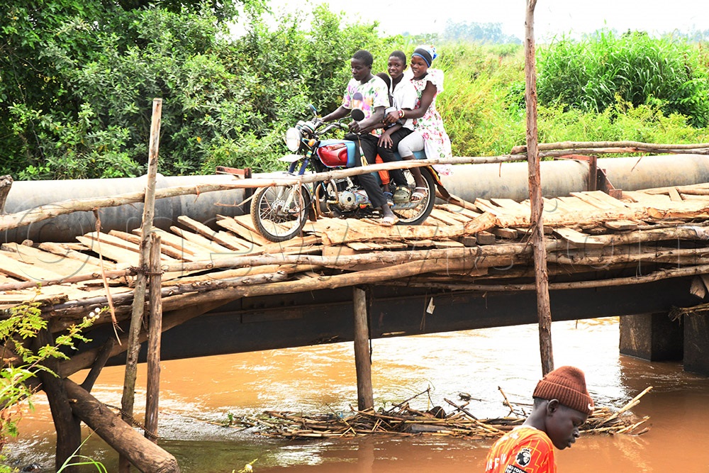 A boda boda cyclist, carrying two passengers crosses River Sironko via a temporary bridge in Tajar village. (Photo by Mpalanyi Ssentongo)