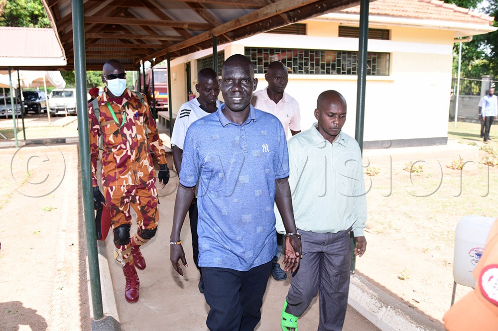 Prison wardens escorting Okedi in handcuffs with Opio, and in the background are Edoket and Obotol as they walk into the courtroom. (Photo by Godfrey Ojore)