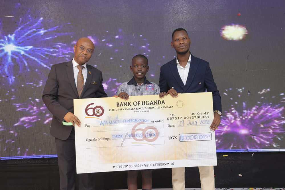 Gibril Rwenzaho of Wakiso Junior School who emerged the overall winner with the dummy check, on the right is Deputy Governor Prof. Augustus Nuwagaba and left is his trainer Peter Bwengye.