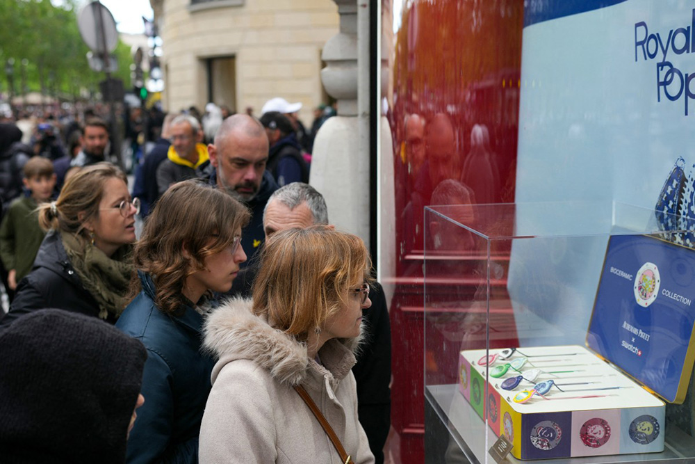 Pedestrians look at displayed watches through a glass window on the facade of a closed shop of Swiss watch company Swatch amid a promotional campaign for their Royal Pop watches in partnership with luxury Swiss watch maker Audemars Piguet in Paris on May 16, 2026. (Photo by Dimitar DILKOFF / AFP)