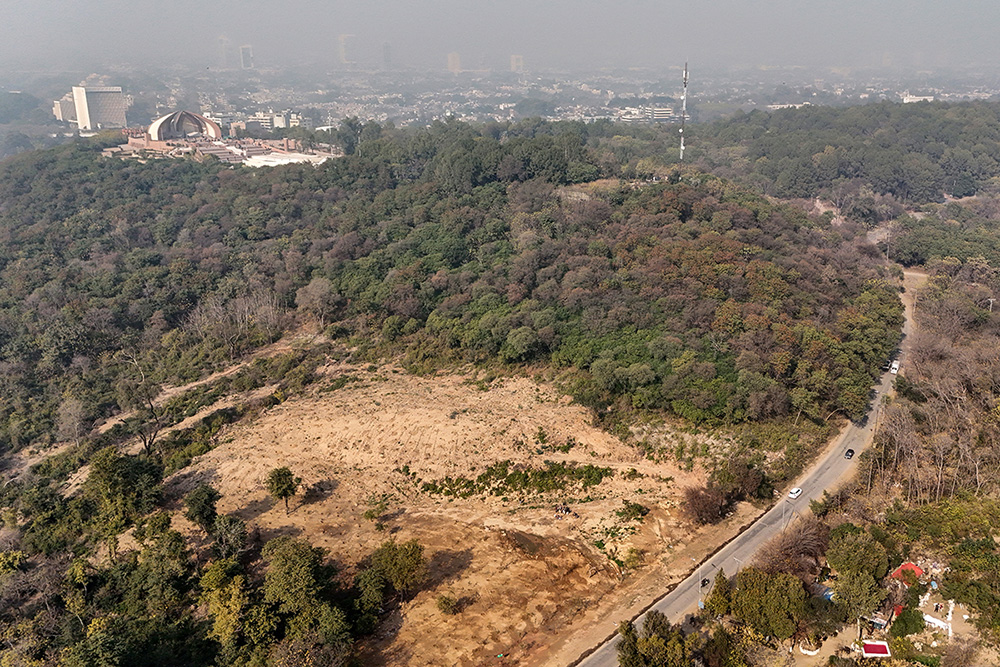 This photograph taken on January 13, 2026 shows an aerial view of commuters driving past a cleared patch (L) of the Shakarparian forest in Islamabad. (Photo by Aamir QURESHI / AFP)