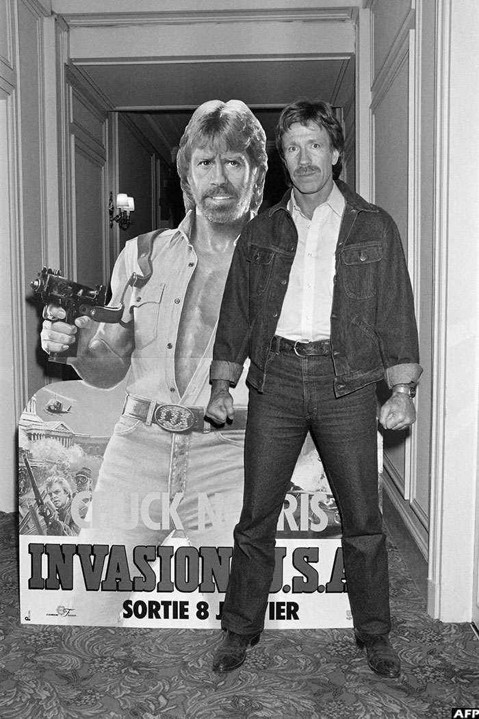Actor Chuck Norris poses on November 27, 1985 in front of the poster for the movie "Invasion USA" at the H&ocirc;tel Plaza Ath&eacute;n&eacute;e in Paris