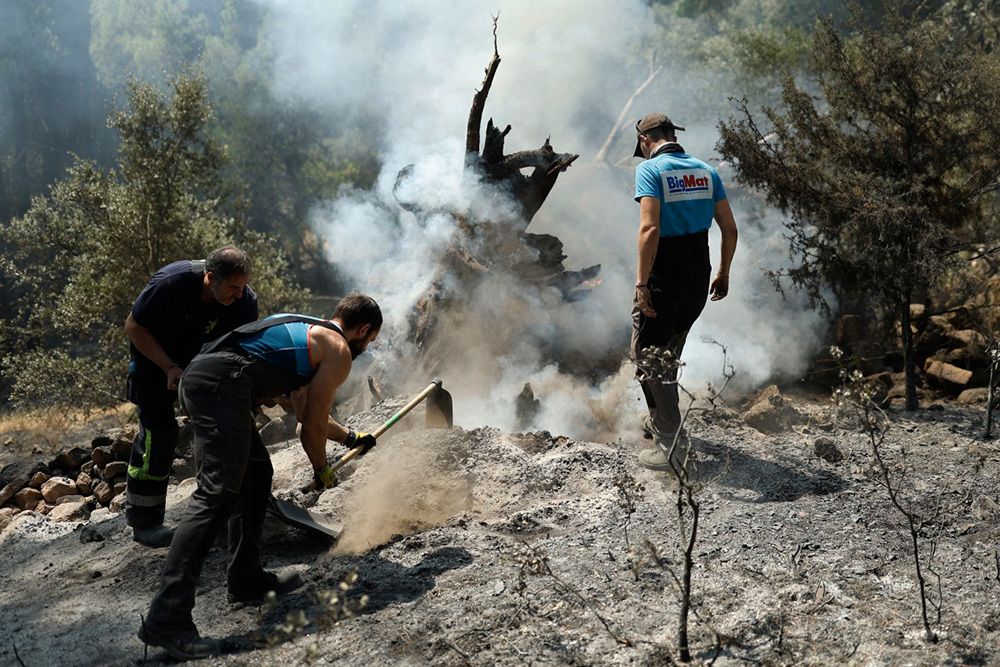 Residents smother embers with dirt to prevent reignition after a wildfire was brought under control near La Adrada, 95 kilometres west of Madrid, on July 28, 2026. (Photo by Oscar DEL POZO / AFP)