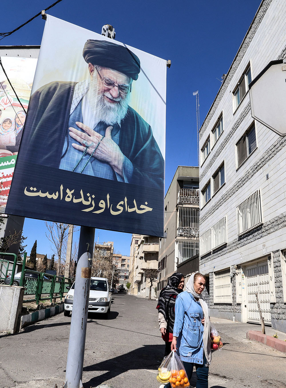 Iranians walk past a portrait of Iran&rsquo;s slain supreme leader Ayatollah Ali Khamenei reading in Persian "His God is still alive" in Tehran on March 3, 2026. The US president said the war, which began on February 28, with a strike that killed Iran's supreme leader Ayatollah Ali Khamenei, was going "substantially" ahead of schedule but warned it could go on for more than four weeks. (Credit: AFP)