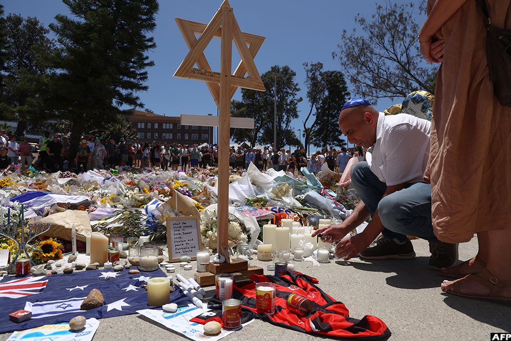 A mourner lights candles as people gather around floral tributes outside Bondi Pavilion in Sydney.