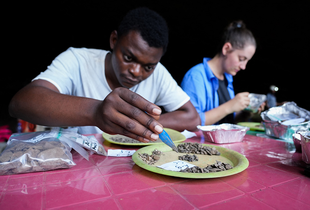 Archaeology students work at a sorting station analyzing sediment samples at Youmbidi Cave in Lastourville, on June 27, 2025. In the heart of Gabon’s equatorial forest, archaeologists are working to reconstruct the prehistory of Central Africa, one careful brushstroke at a time. (Photo by Nao Mukadi / AFP)