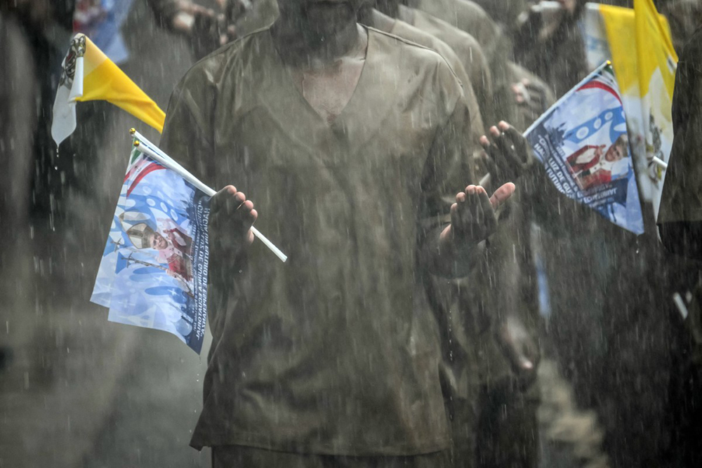Inmates hold flags bearing images commemorating the visit of Pope Leo XIV as they pray in the rain during his visit to Bata Prison in Bata on the tenth day of an 11-day apostolic journey to Africa, on April 22, 2026. (AFP)