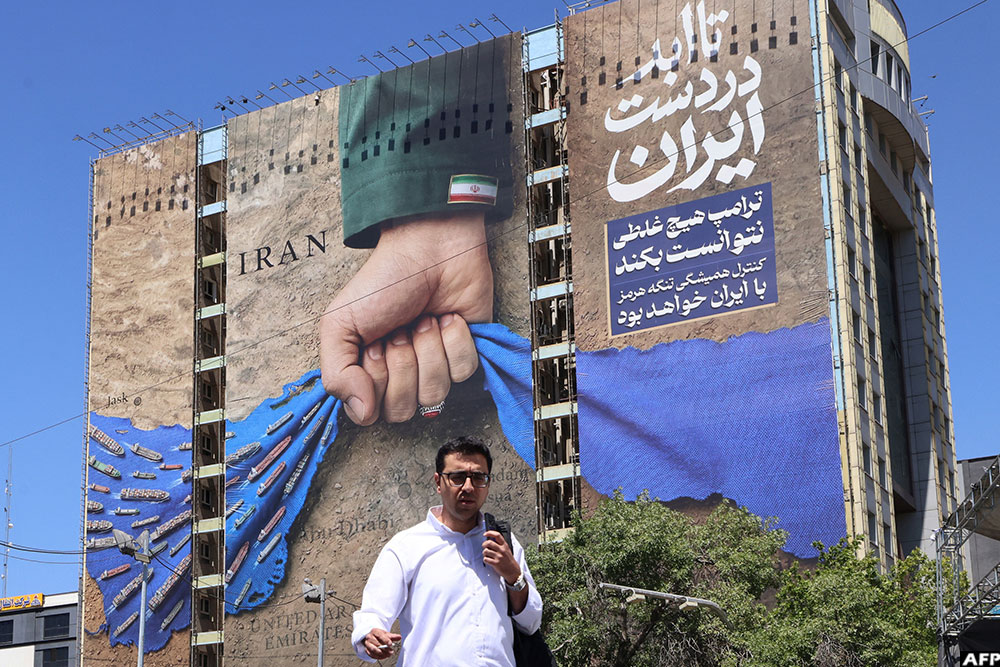 A man crosses a street past a billboard on the facade of a building depicting the Strait of Hormuz with a caption in Persian reading "Forever in Iran’s Hand", at Vanak Square in Tehran on May 25, 2026
