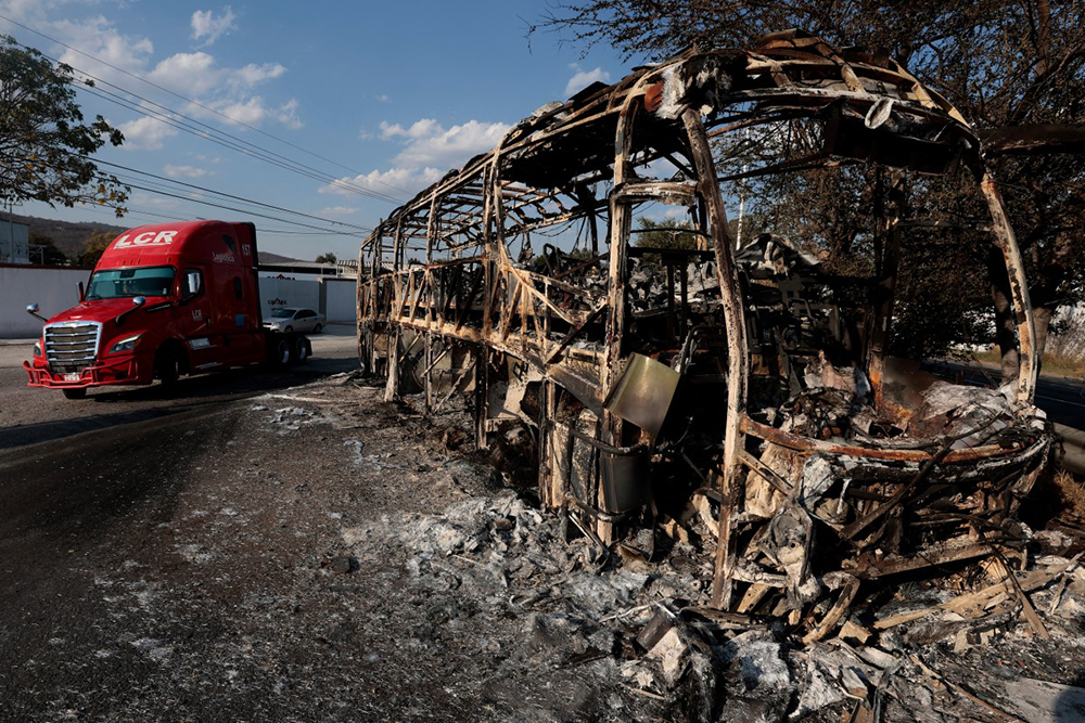 A truck unit passes by a burned bus, allegedly set on fire by organised crime groups in response to an operation to arrest a high-priority security target, on a highway near Acatlan de Juarez, Jalisco state, Mexico on February 22, 2026. (Credit: AFP)