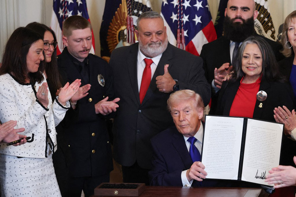 U.S. President Donald Trump, surrounded by family members who have lost a relative to a crime committed by an undocumented immigrant, holds up a proclamation dedicating February 22nd as Angel Family Day during a remembrance ceremony held in the East Room at the White House February 23, 2026 in Washington, DC. (Credit: AFP)