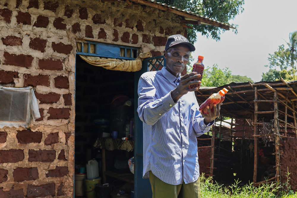 Stephen Munga, 59, a local bee farmer emerges with bottles of organic honey harvested from some of his traditional bee hives set up in the Mrima Hill Forest, from one of the houses in his homestead on the periphery of forest in Lunga-Lunga, Kwale county on September 26, 2025. (Photo by Tony KARUMBA / AFP)