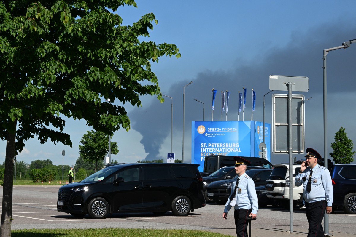 Police officers walk in front of banners with branding for the St. Petersburg International Economic Forum (SPIEF) at the forum's venue as black smoke rises in distance in Saint Petersburg on June 3, 2026. (Credit: AFP)