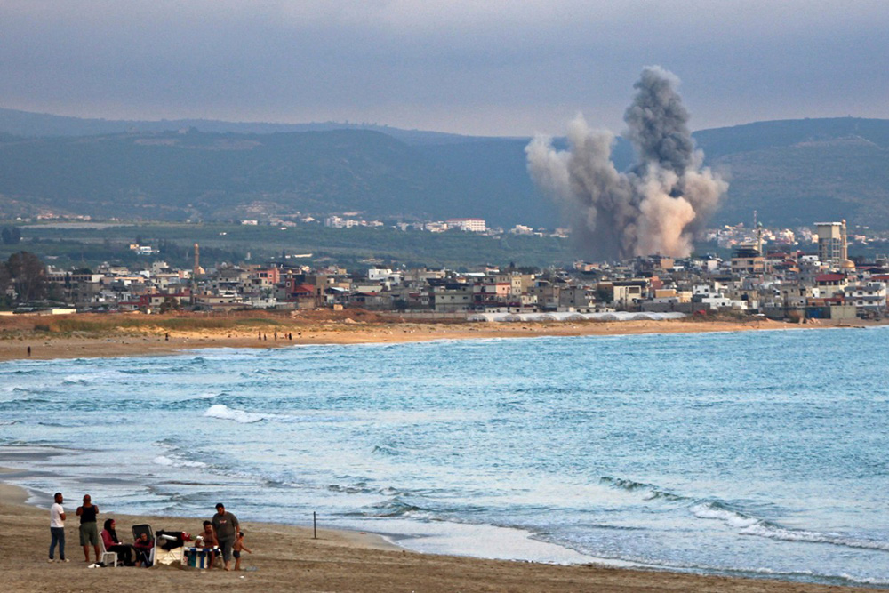 People visit a beach against the backdrop of smoke rising from the site of an Israeli strike near the southern Lebanese city of Tyre on May 27, 2026.(Photo by KAWANT HAJU / AFP)