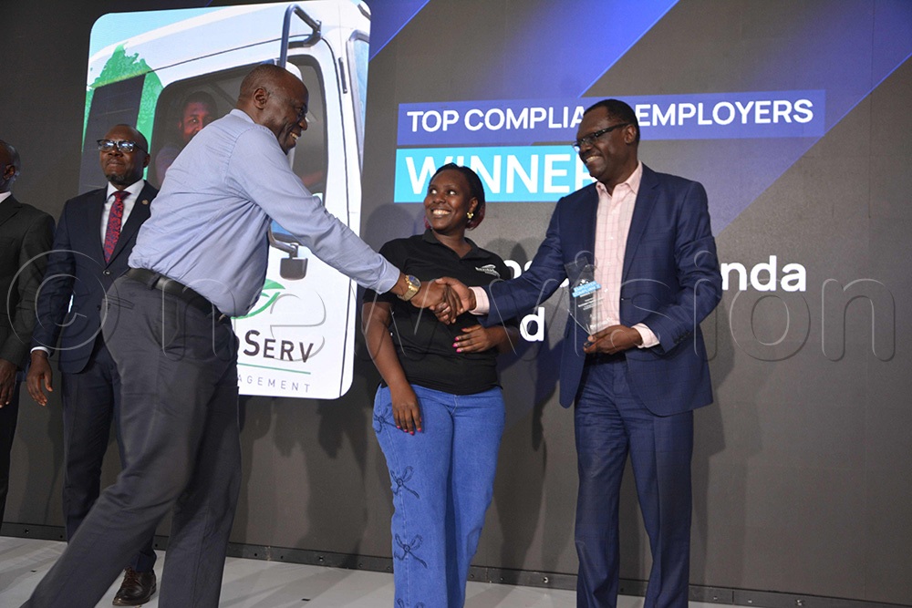 Patrick Ayota, the Managing Director NSSF, (R) giving top best compliance award to EnviroServ staff led by James Sseruyange (L) after the meeting. (Photo by Peter Abaanabasazi)