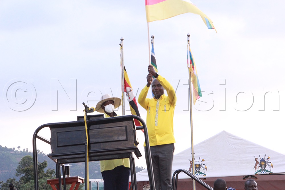 The Minister of State for Finance, Planning and Economic Development (General Duties), also member of Parliament, Rubanda East Constituency, Hon. Henry Musasizi, waving the NRM flag as an aspirant for the next parliamentary election, as Museveni looks on. (Credit:  Nelson Ahimbisibwe)