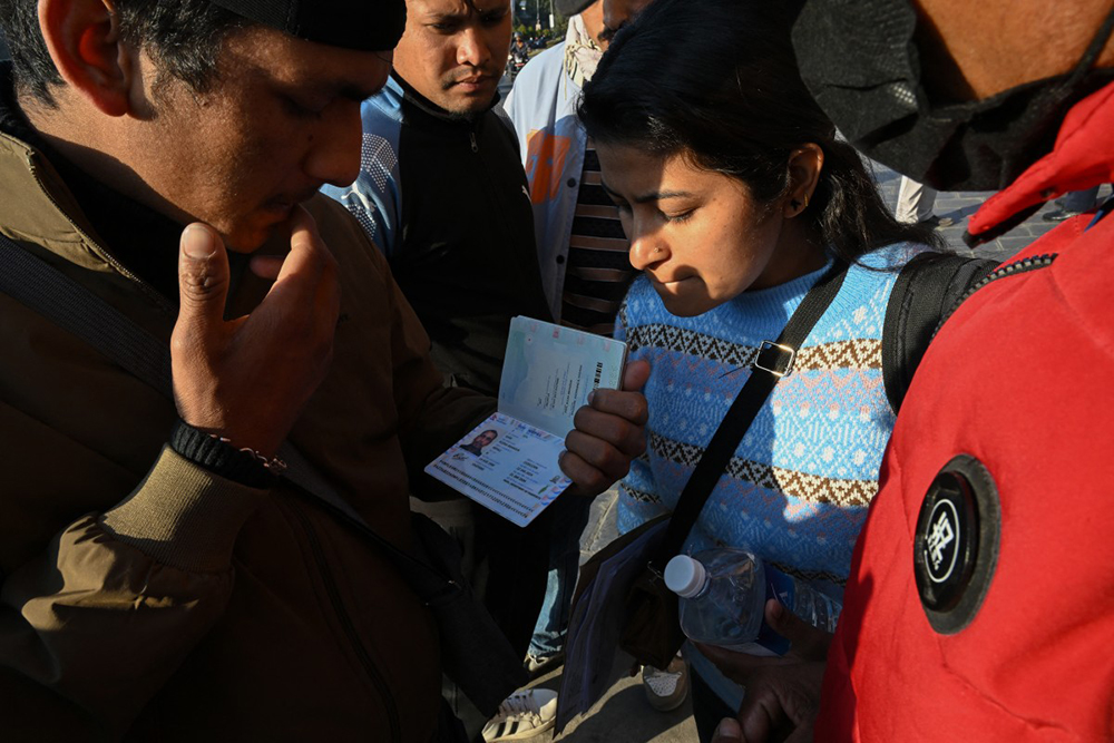 This photograph taken on January 21, 2026 shows Lalit Bishowkarma (L), son of migrant worker Rudra Bahadur Kami, looking at his father's passport with a relative as they wait for the arrival of Kami's body outside Tribhuvan International Airport in Kathmandu. 